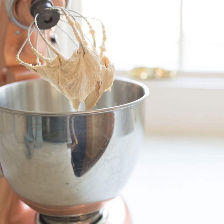 caramel icing in a silver mixing bowl on a stand mixer.