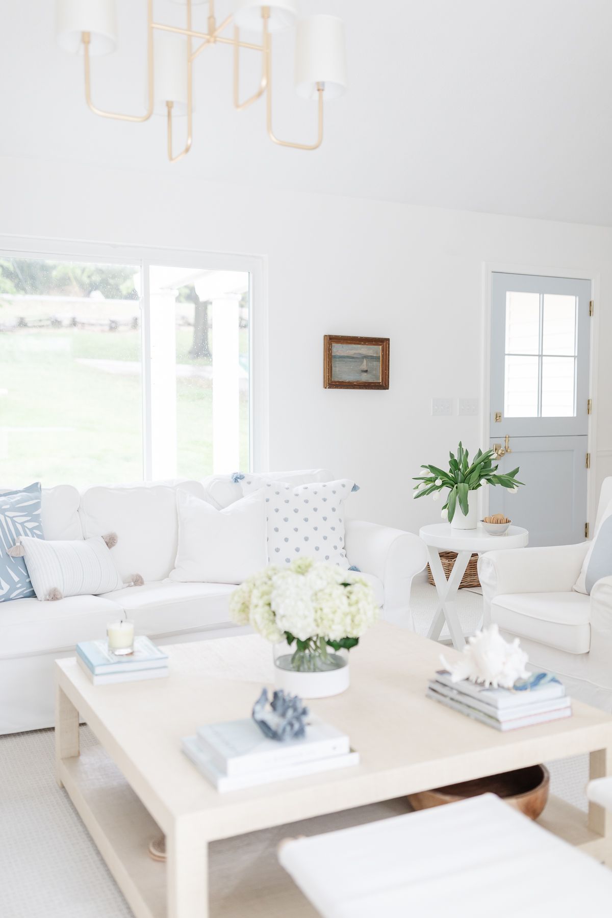 A coastal inspired white living room with a beige linen square coffee table in the center.