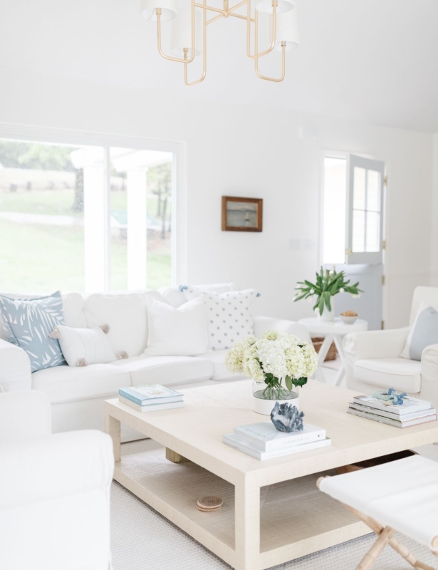 A coastal inspired white living room with a beige linen square coffee table in the center.
