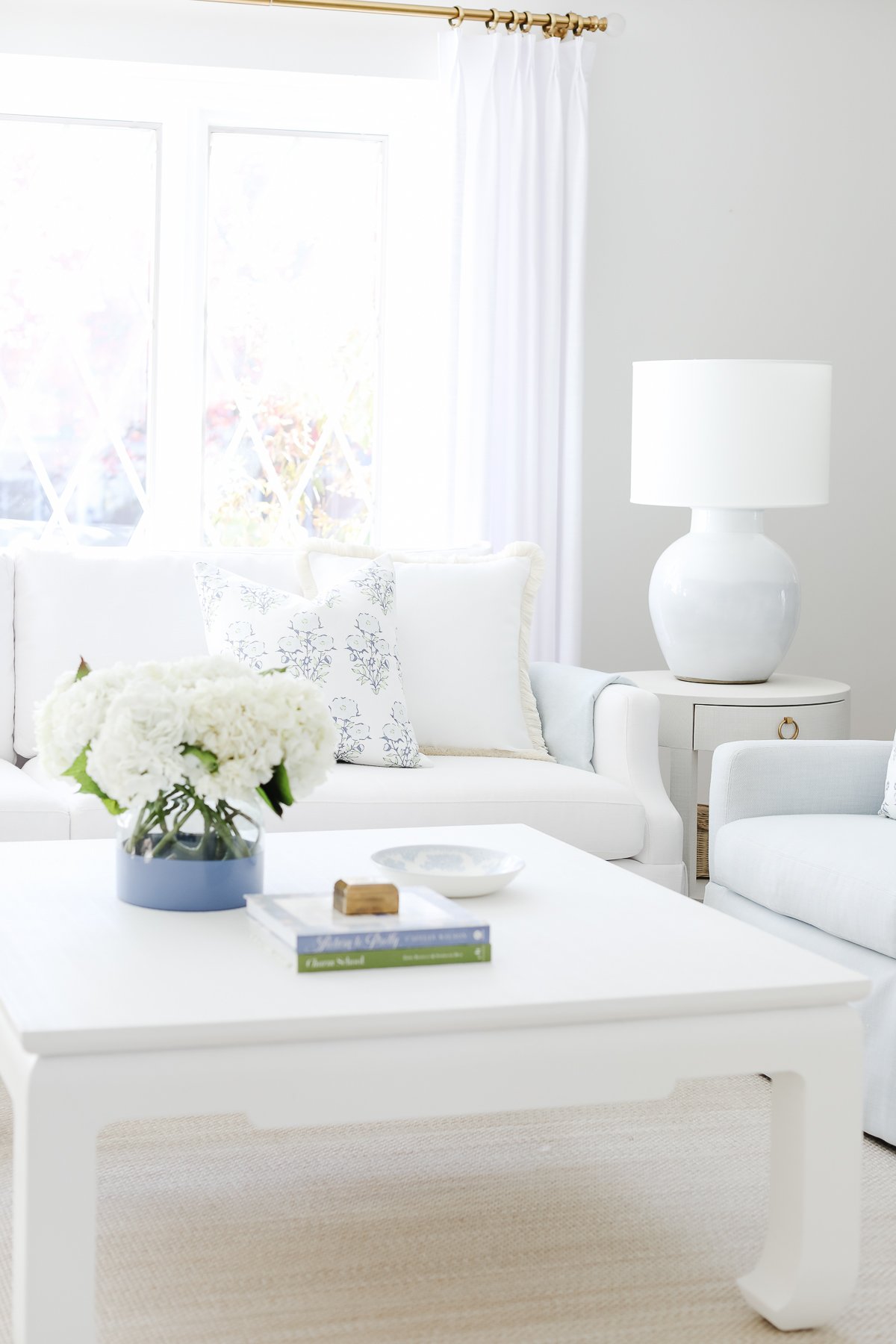 Bright living room with white furniture, a coffee table of perfect height, and floral accents near a window.