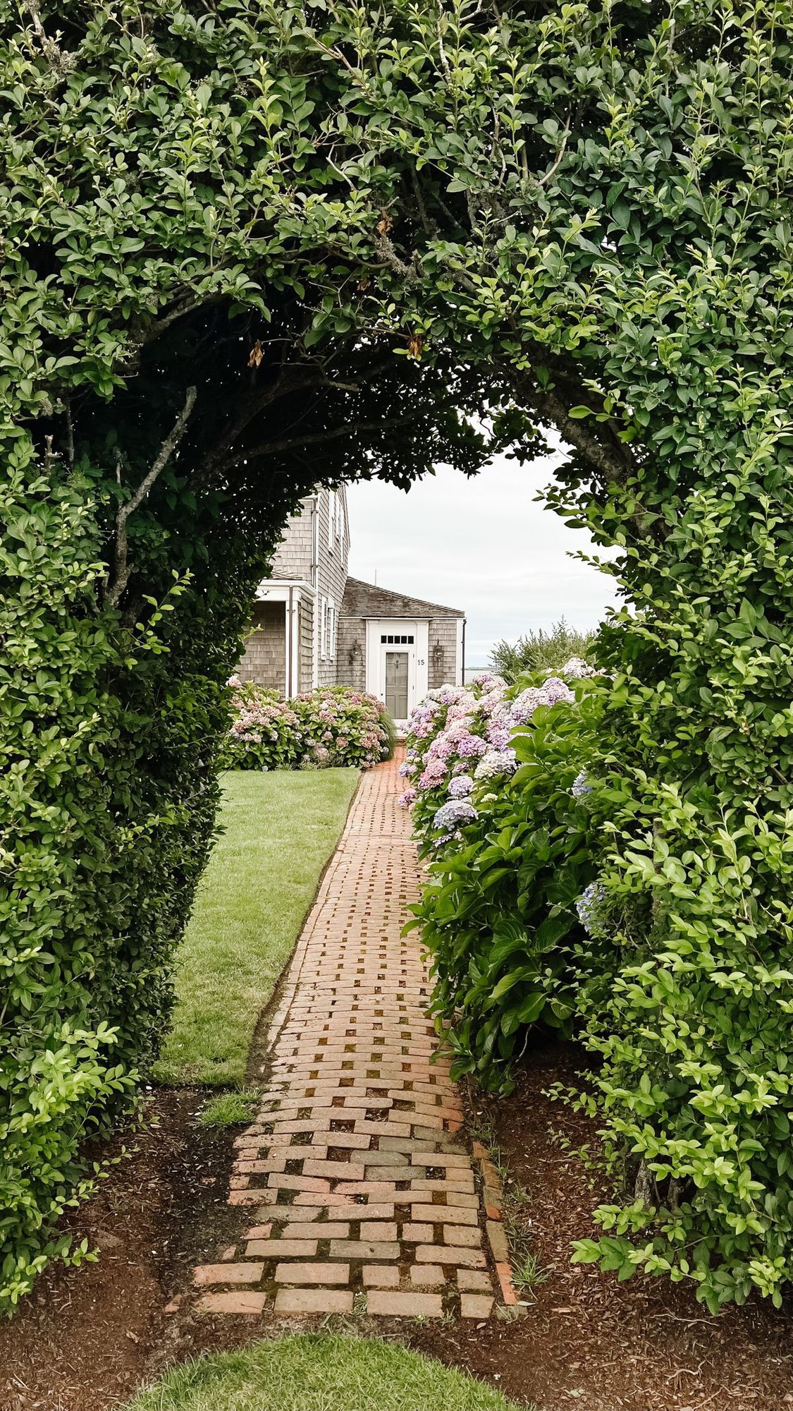 A cobblestone walkway surrounded by arched greenery in a Nantucket guide