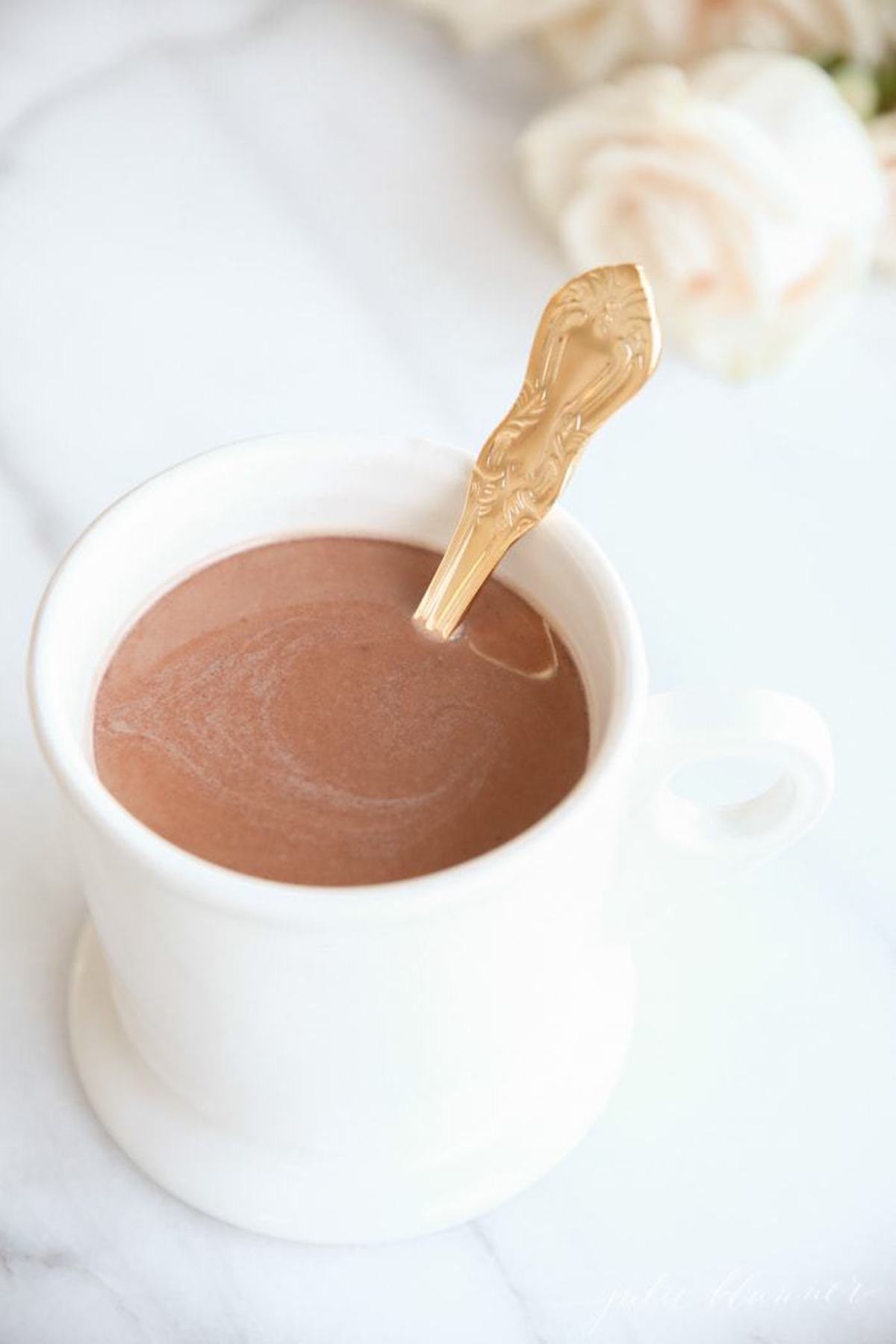 hot chocolate in a white mug, with a gold spoon for stirring