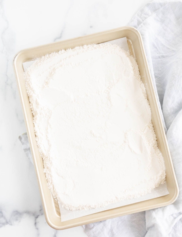 Flour spread out on a gold rimmed baking sheet, on a marble countertop