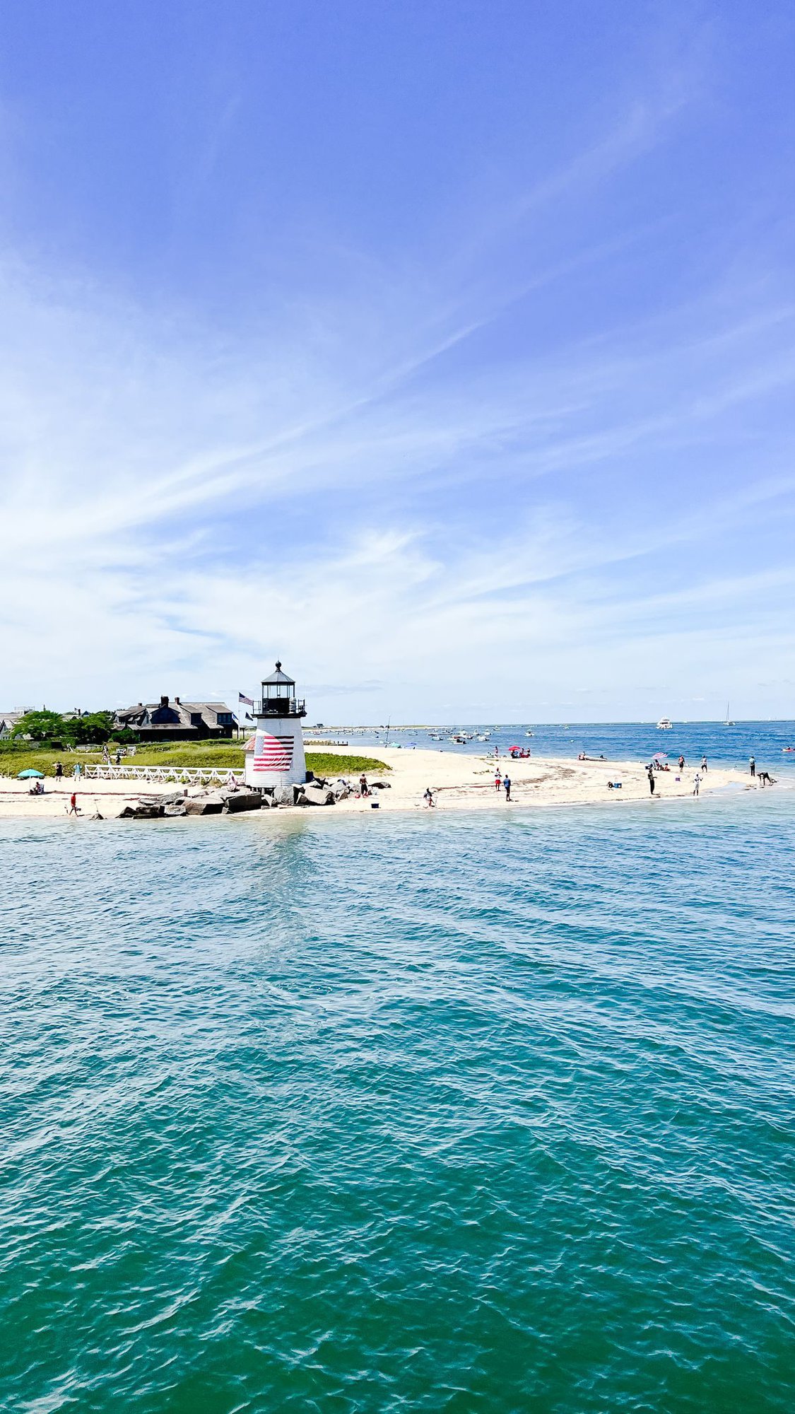 A beach scene, taken from the water, with a lighthouse on the island of Nantucket