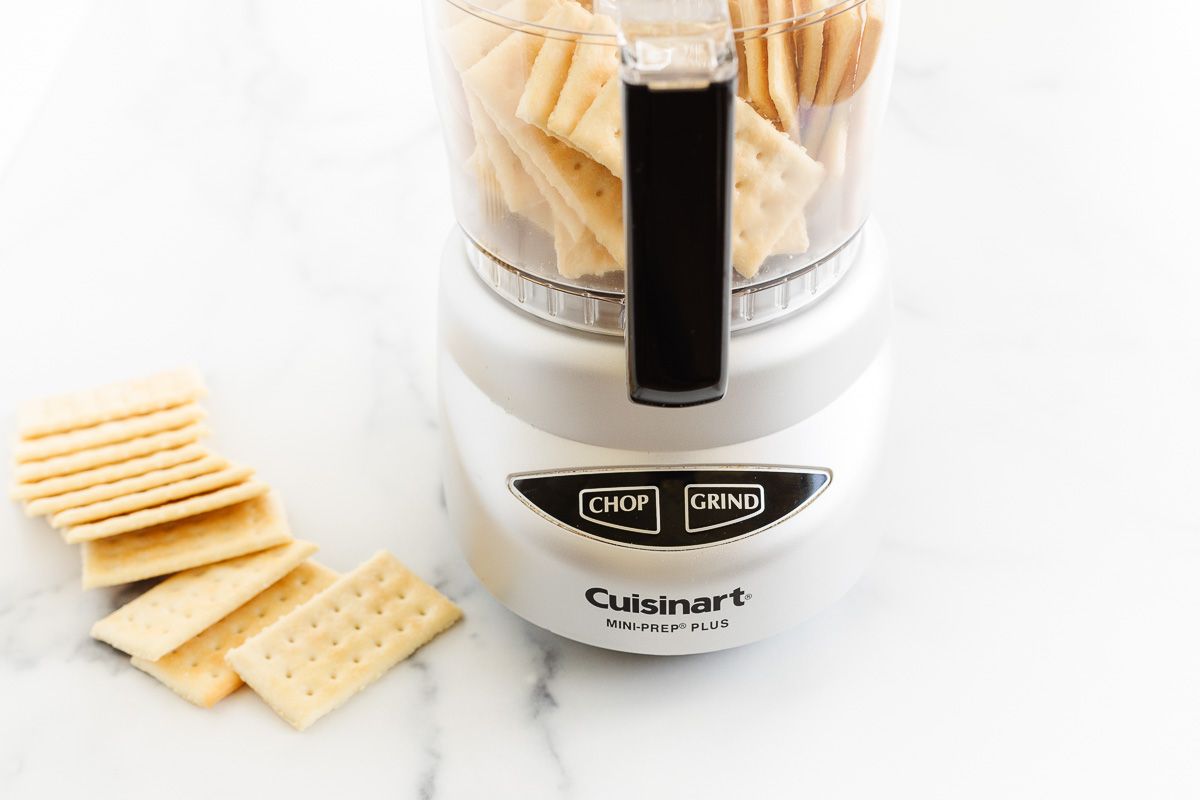 Club crackers in and around a small food processor, on a marble countertop.
