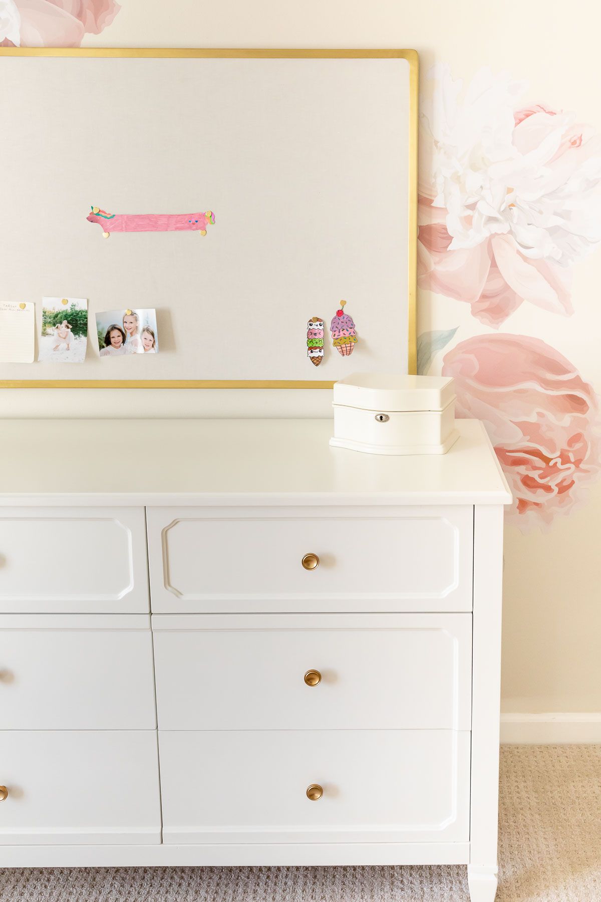 A girl's bedroom with cream walls and peony wall decals behind a white dresser.