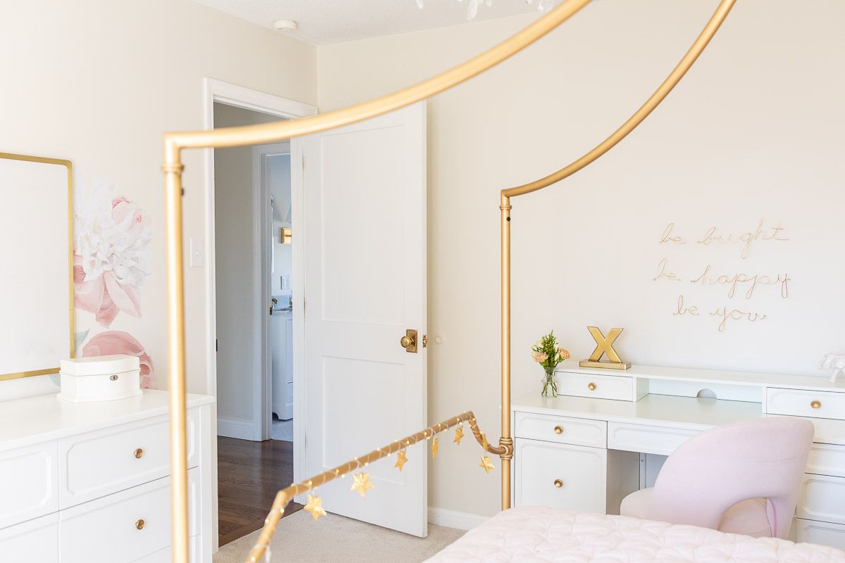 A girl's bedroom with a gold canopy bed and peony wallpaper on one wall