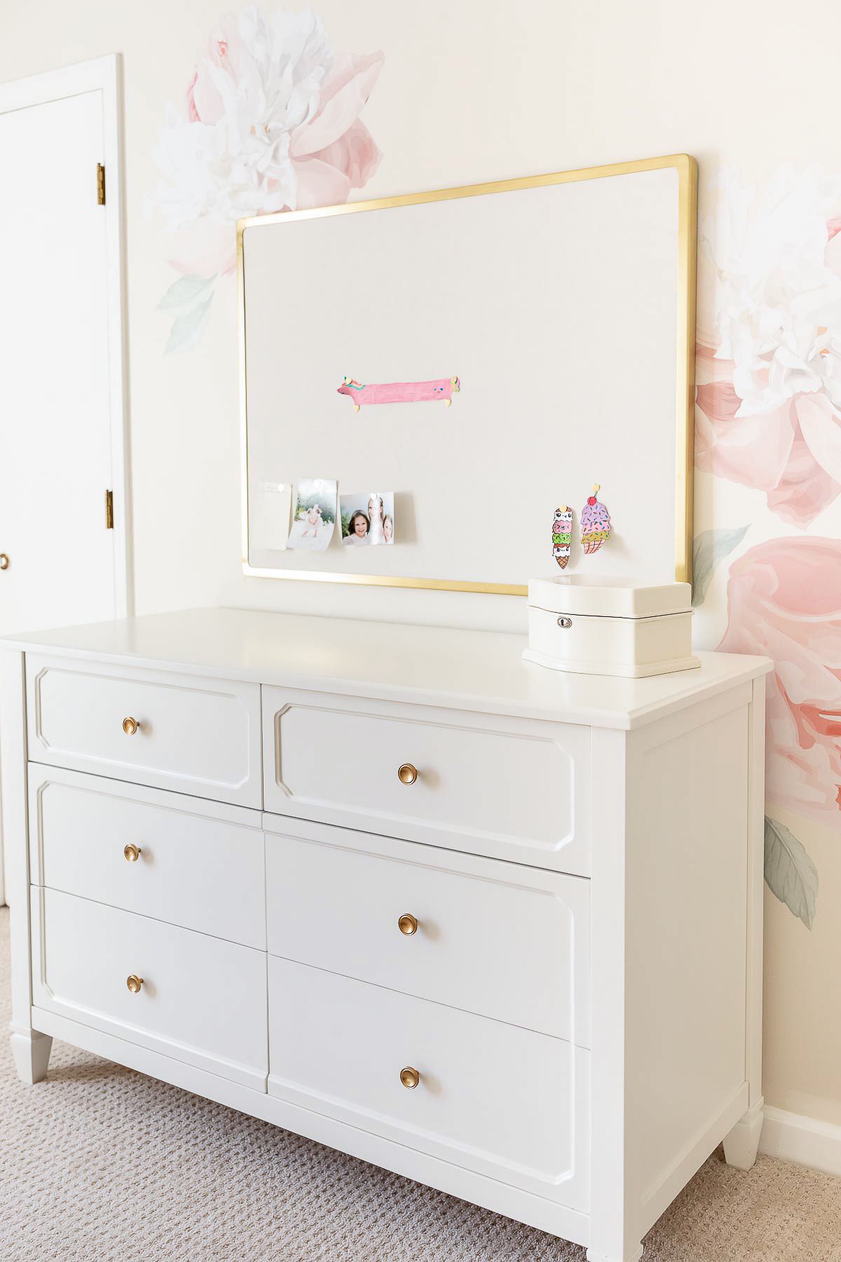 A girl's bedroom with cream walls and peony flower wallpaper behind a white dresser.