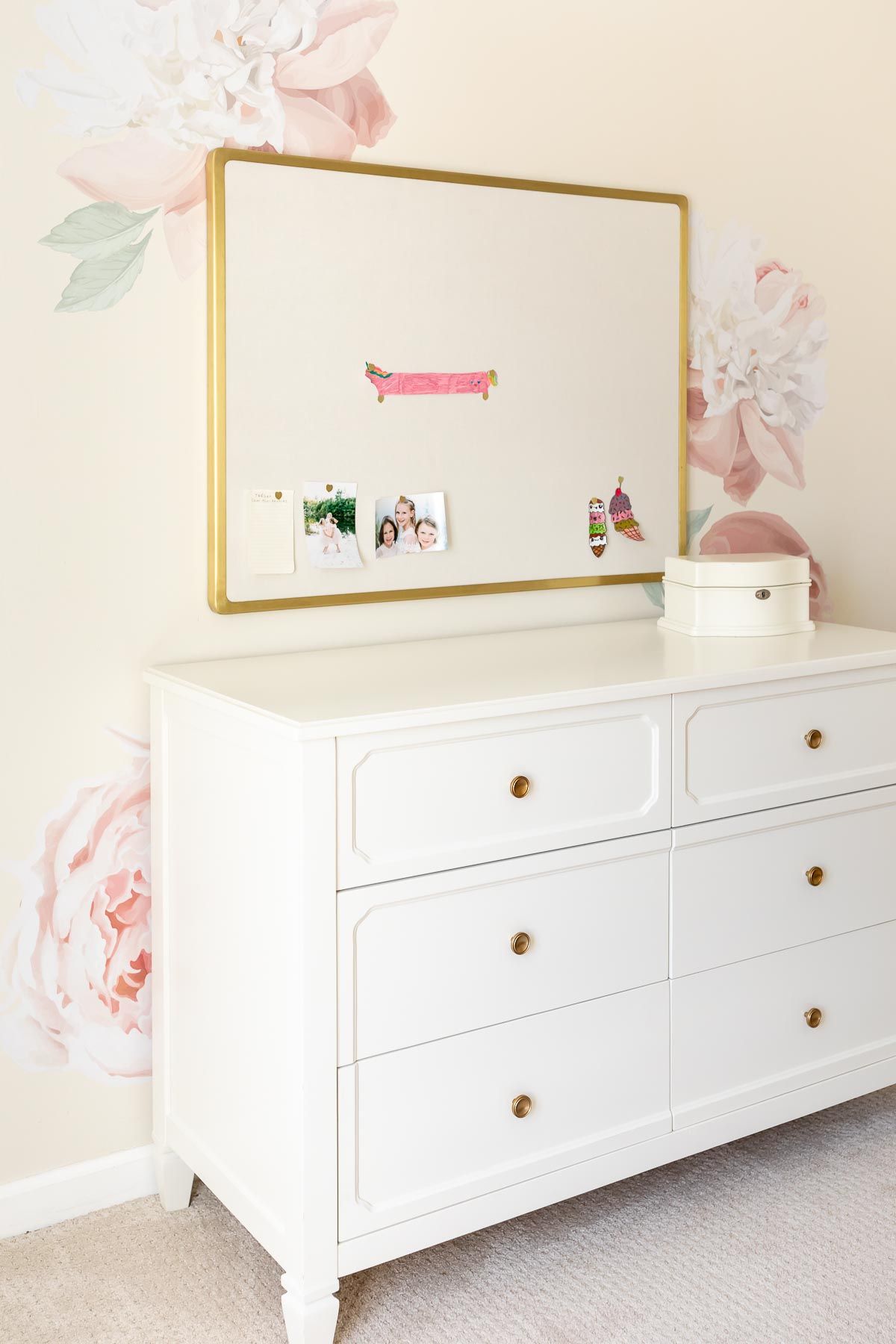 A girl's bedroom with cream walls and peony wallpaper behind a white dresser.