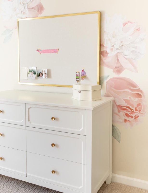 A girl's bedroom with cream walls and peony wallpaper behind a white dresser.
