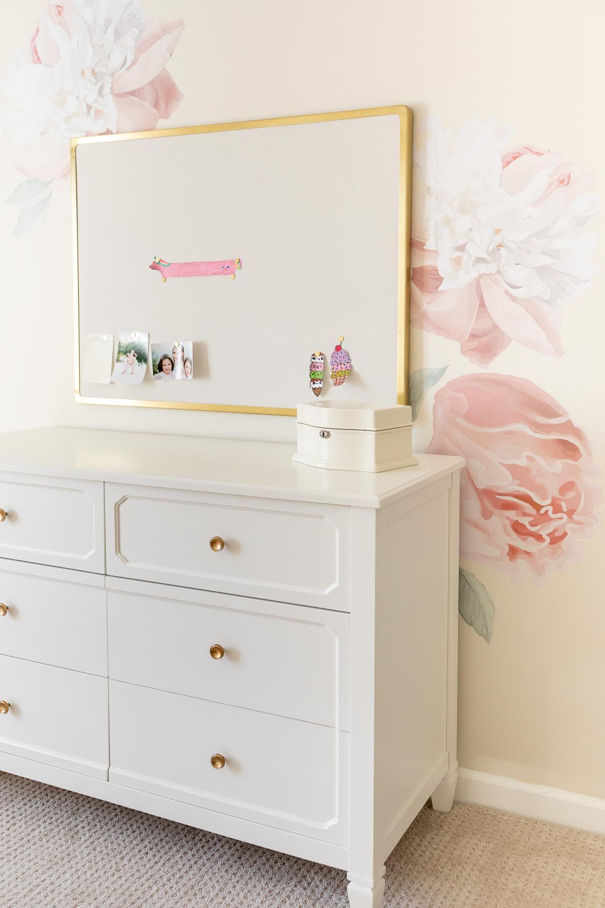 A girl's bedroom with cream walls and peony wallpaper behind a white dresser.