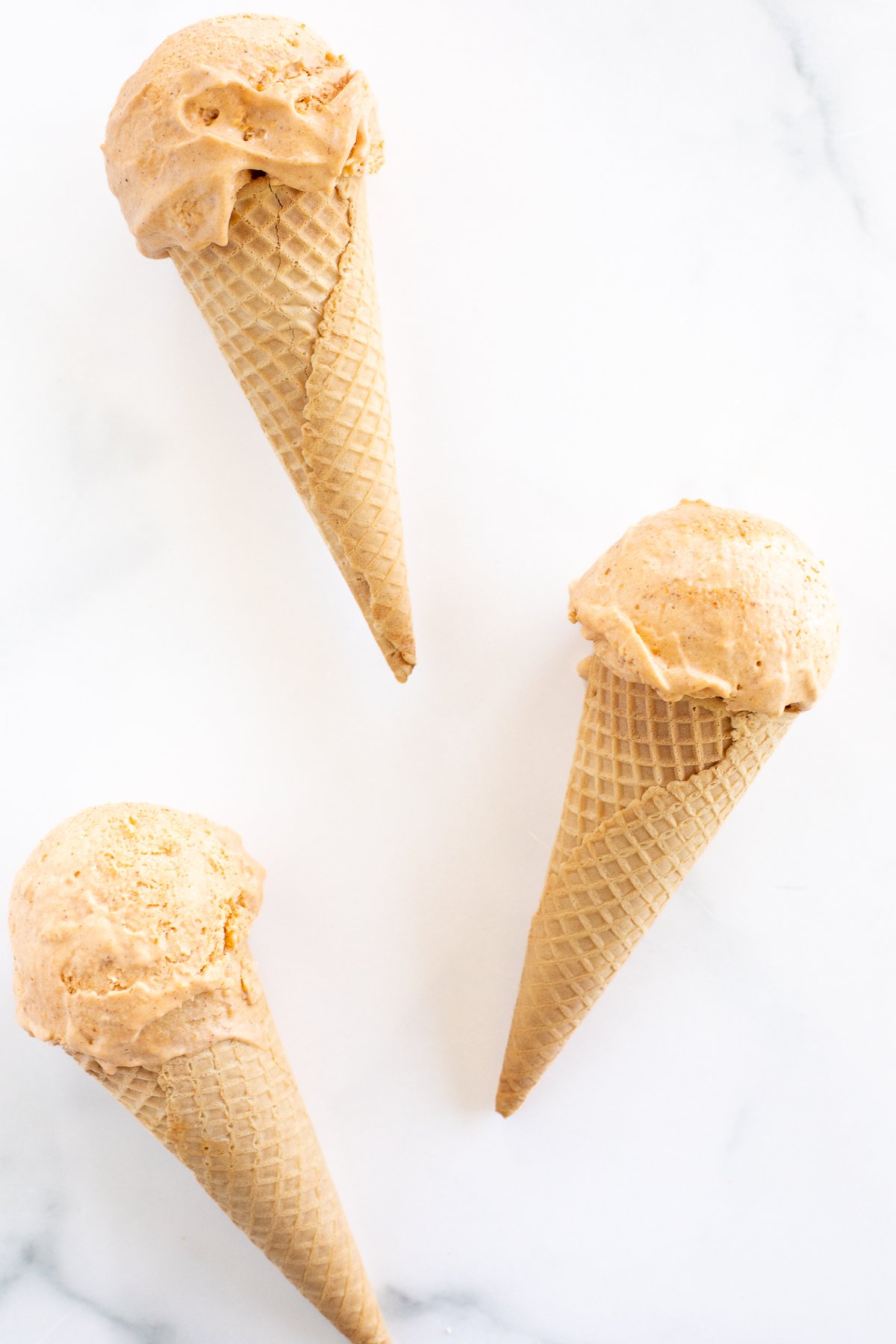 Three peanut butter ice cream cones on a marble surface, perfect for pumpkin desserts.