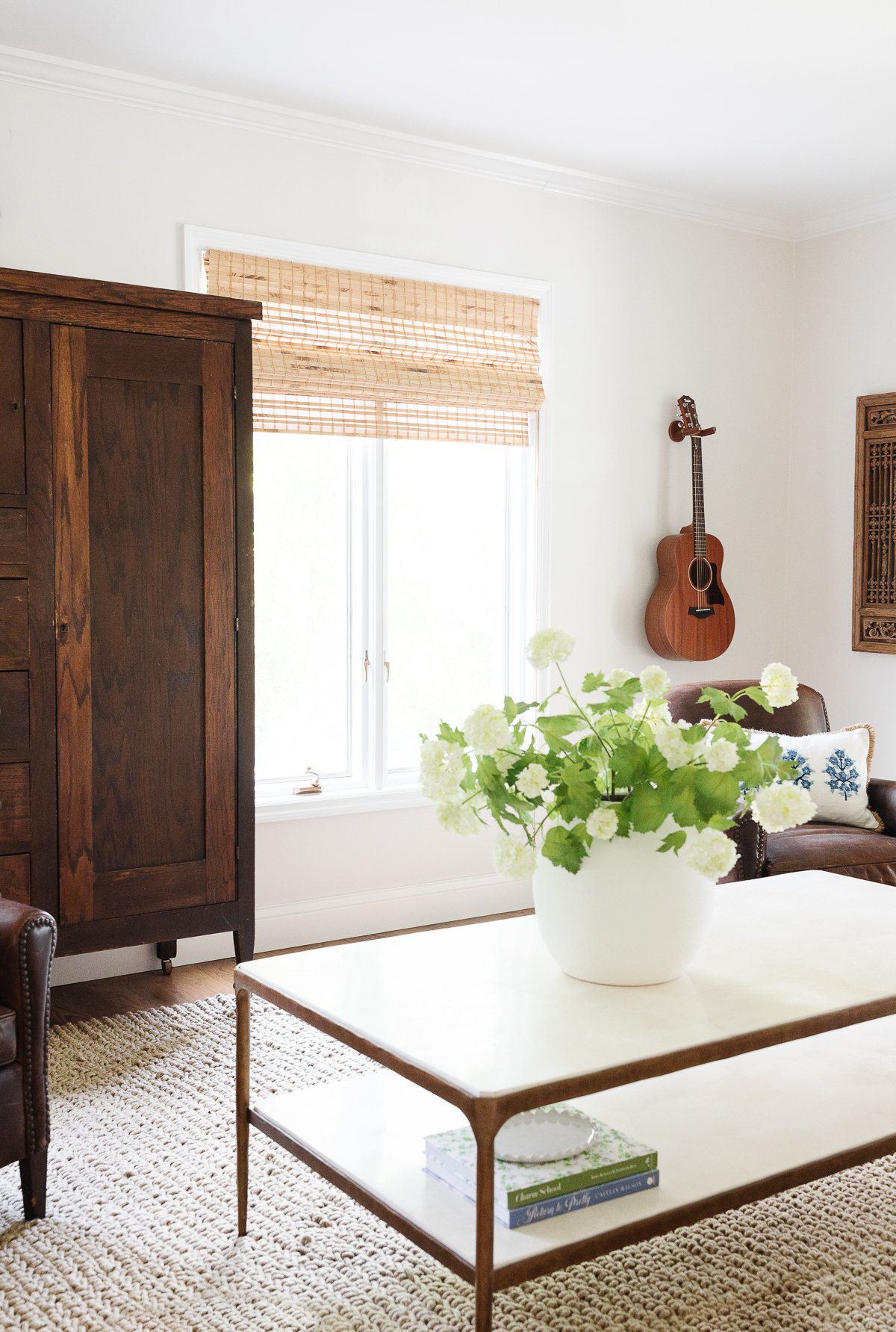 A bright living room featuring a wooden cabinet, a ukulele on the wall, a glass-top coffee table with dimensions suitable for the available space and ideal height for comfort, with a book, and
