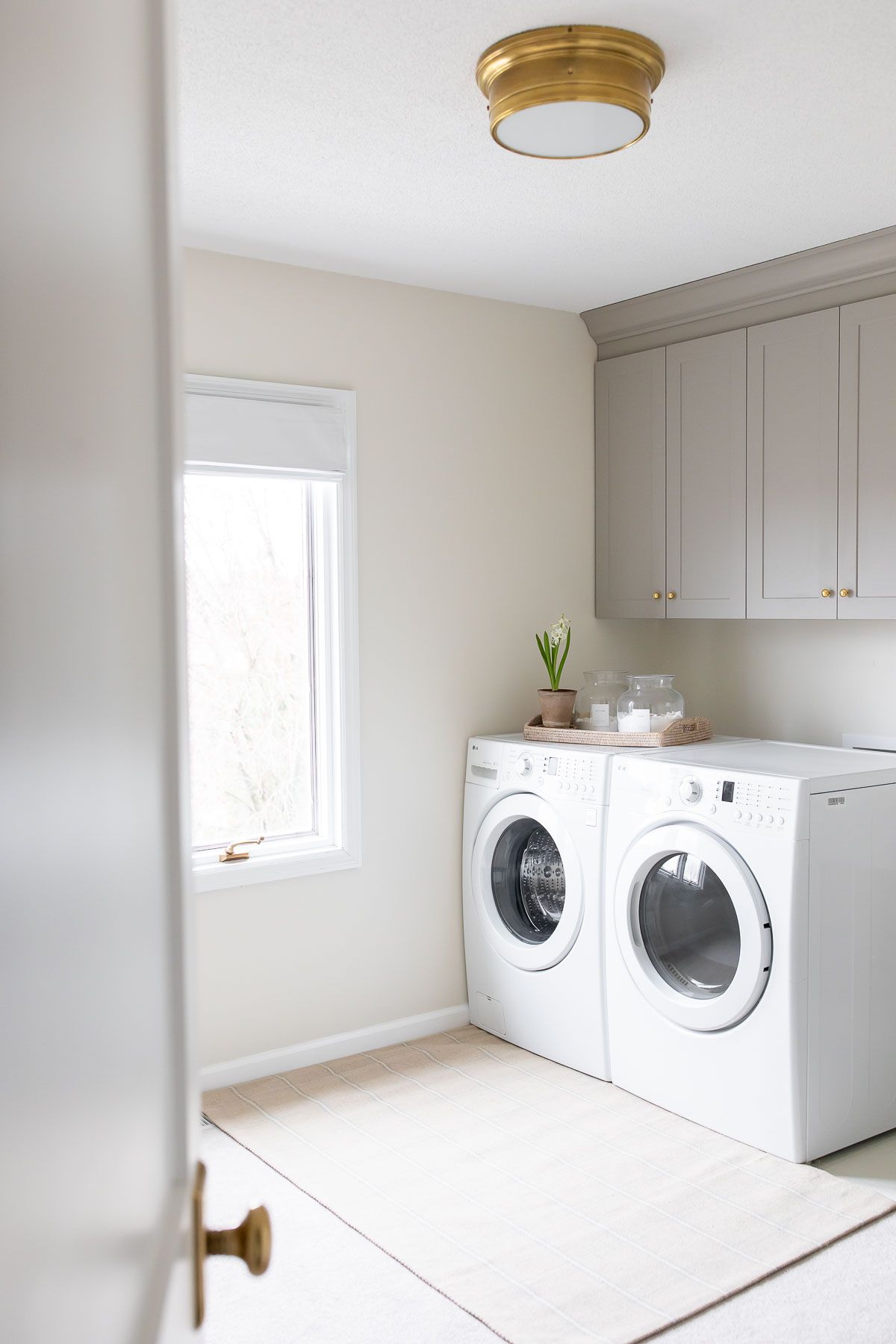 A laundry room with gray cabinets, white washer and dryer, and a plaid rug on carpet.