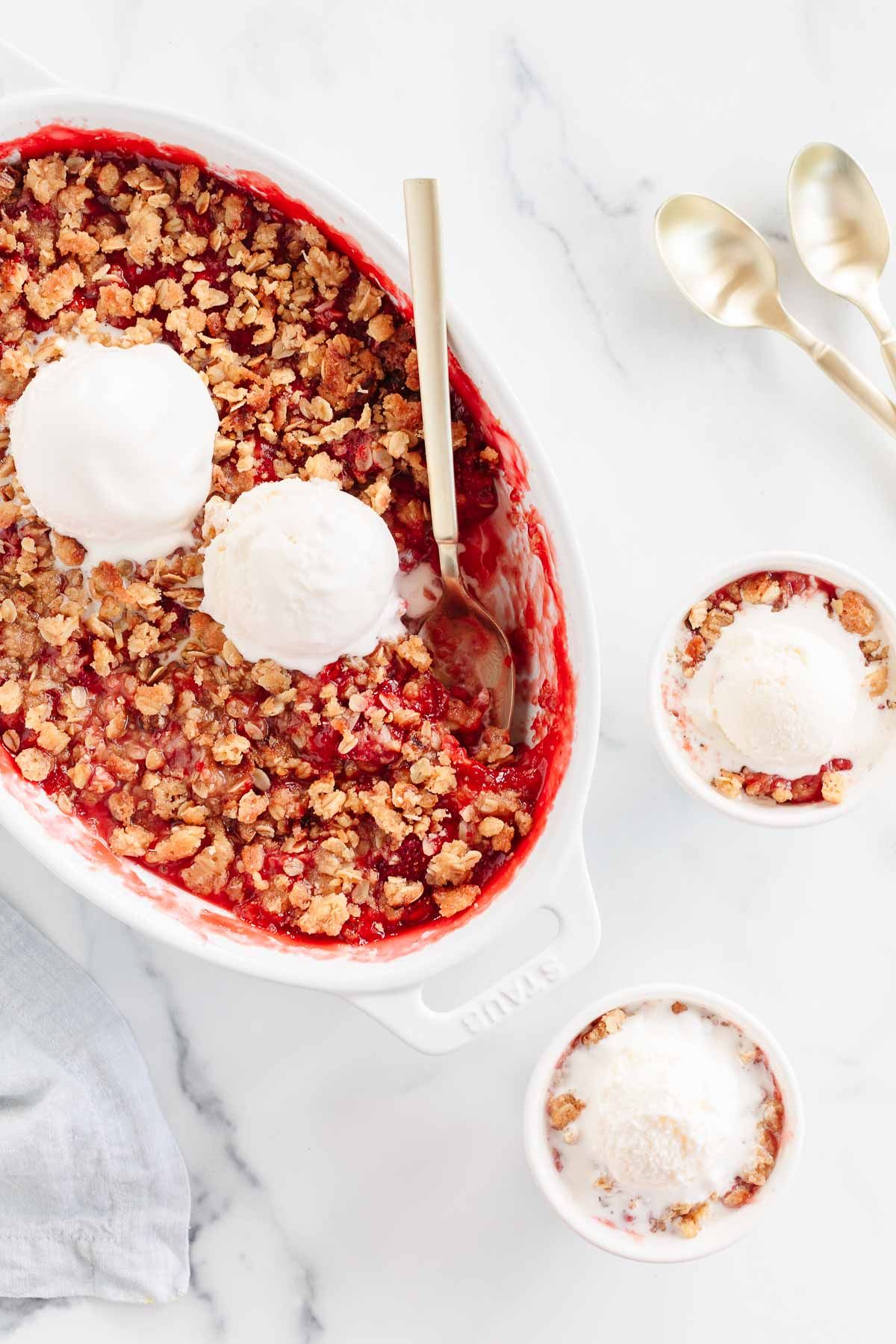 Strawberry crumble topped with vanilla ice cream in a small bowl, baking dish in the background