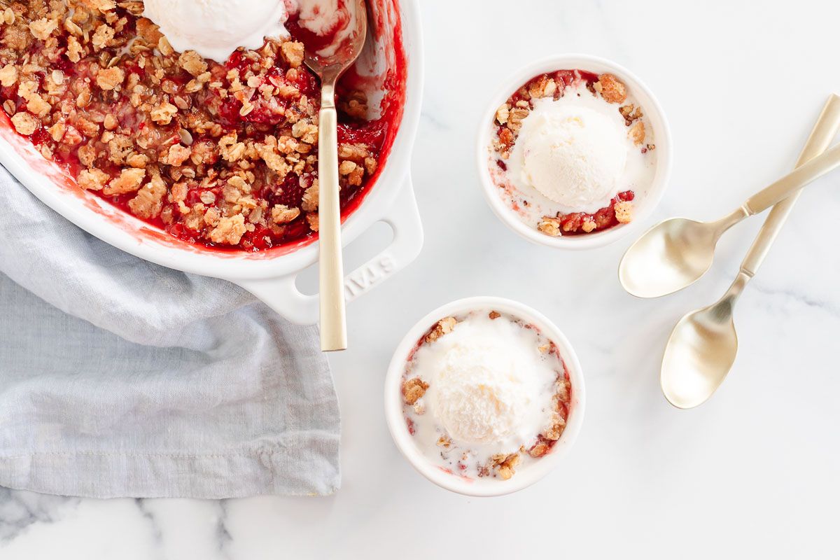 Strawberry crumble topped with vanilla ice cream in a small bowl, baking dish in the background