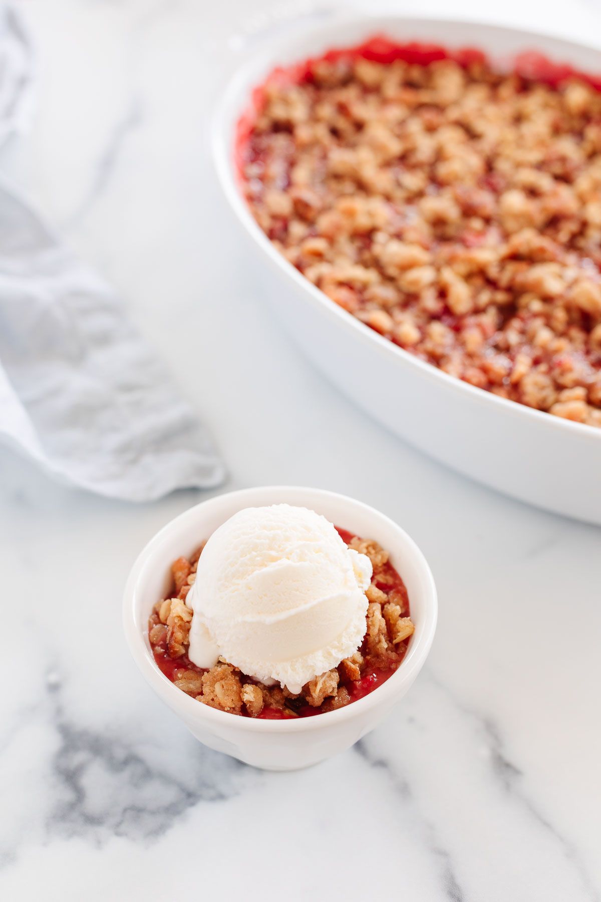 Strawberry crumble topped with vanilla ice cream in a small bowl, baking dish in the background