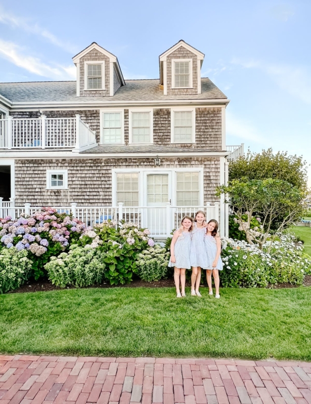 Three little girls in blue dresses in front of a shingled cottage on Nantucket