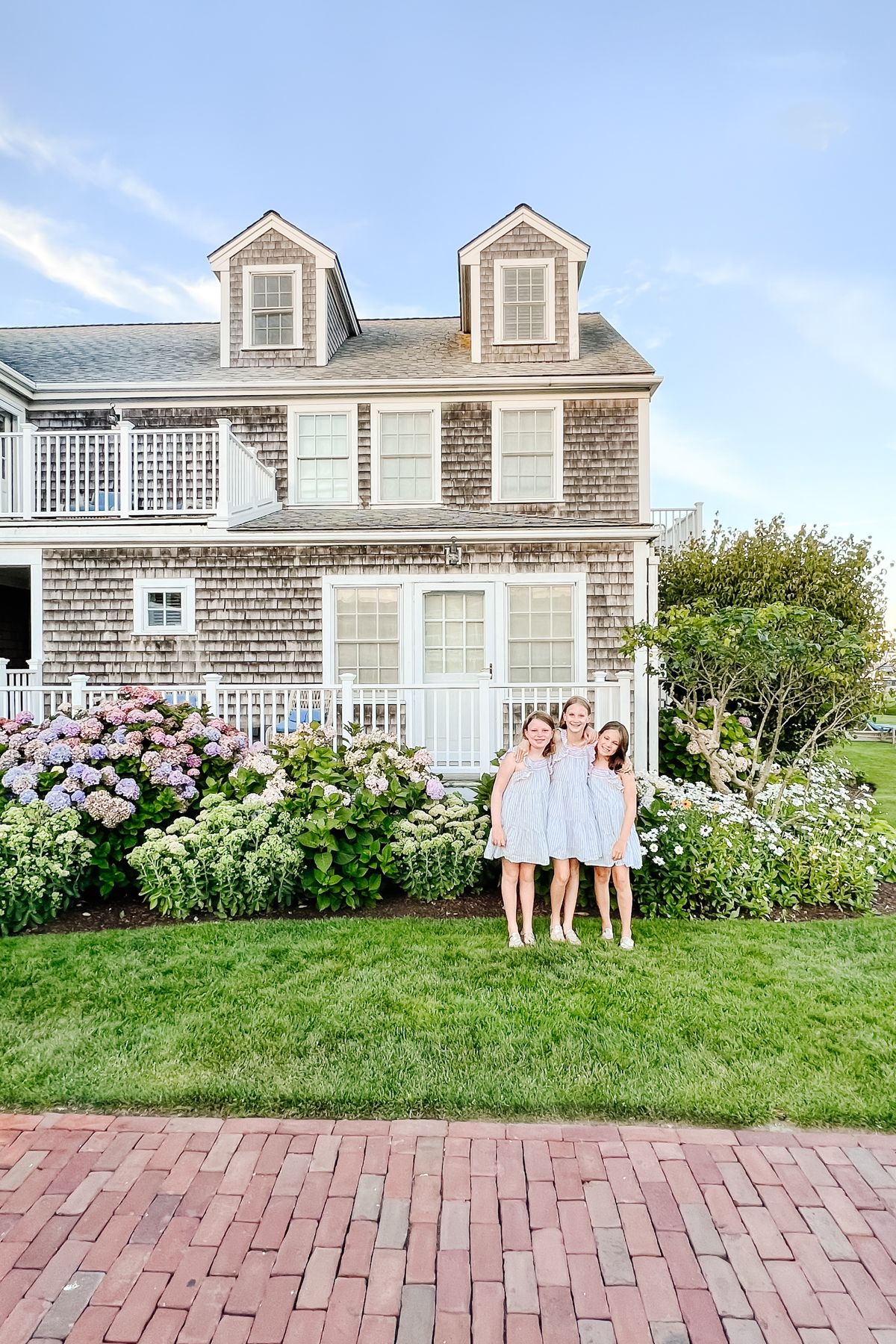 Three little girls in blue dresses in front of a shingled cottage on Nantucket