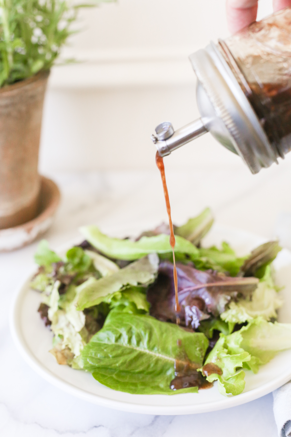 A bottle of vinaigrette dressing being poured over a plate of salad. 