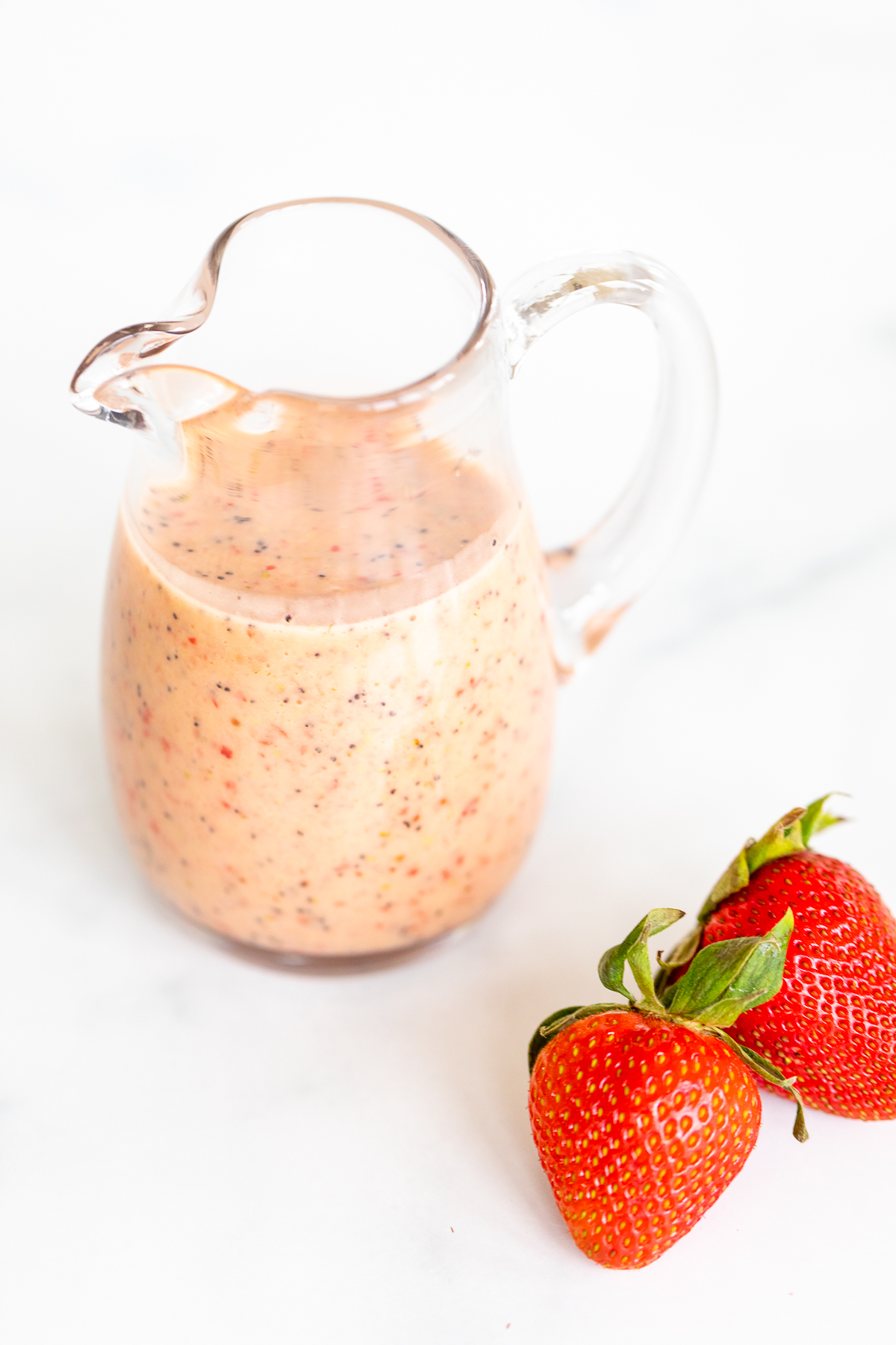 A glass jar of poppyseed dressing, with fresh strawberries next to it. 