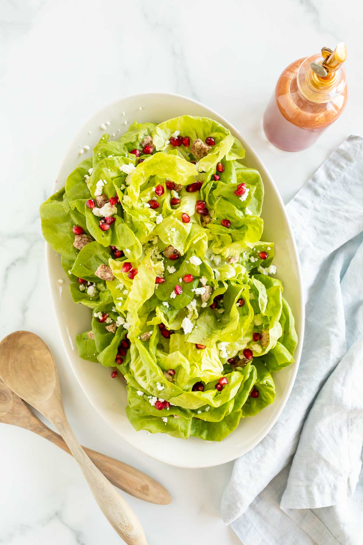 A pomegranate salad in a white oval bowl, with a bottle of homemade vinaigrette dressing next to it. 