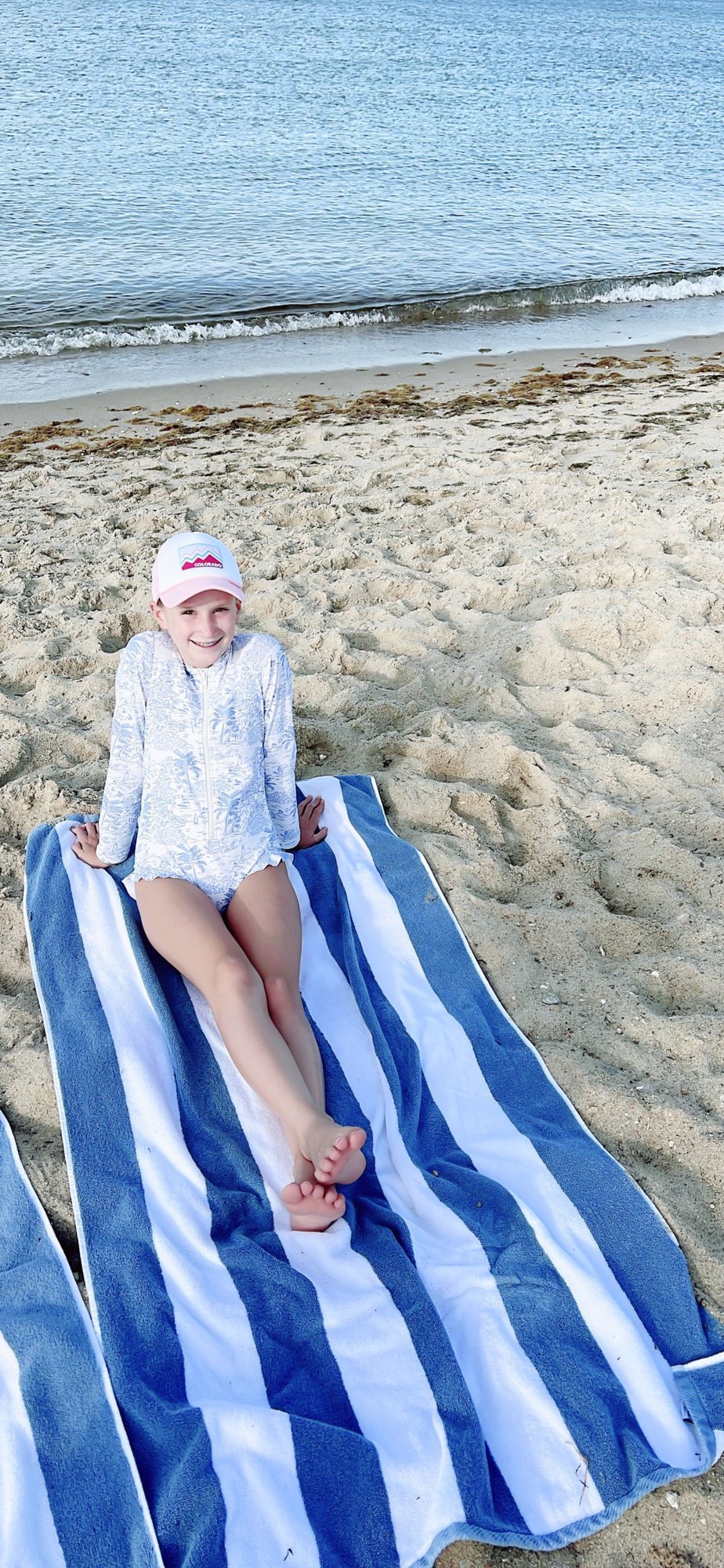 A little girl on a blue and white striped towel on a martha's vineyard beach