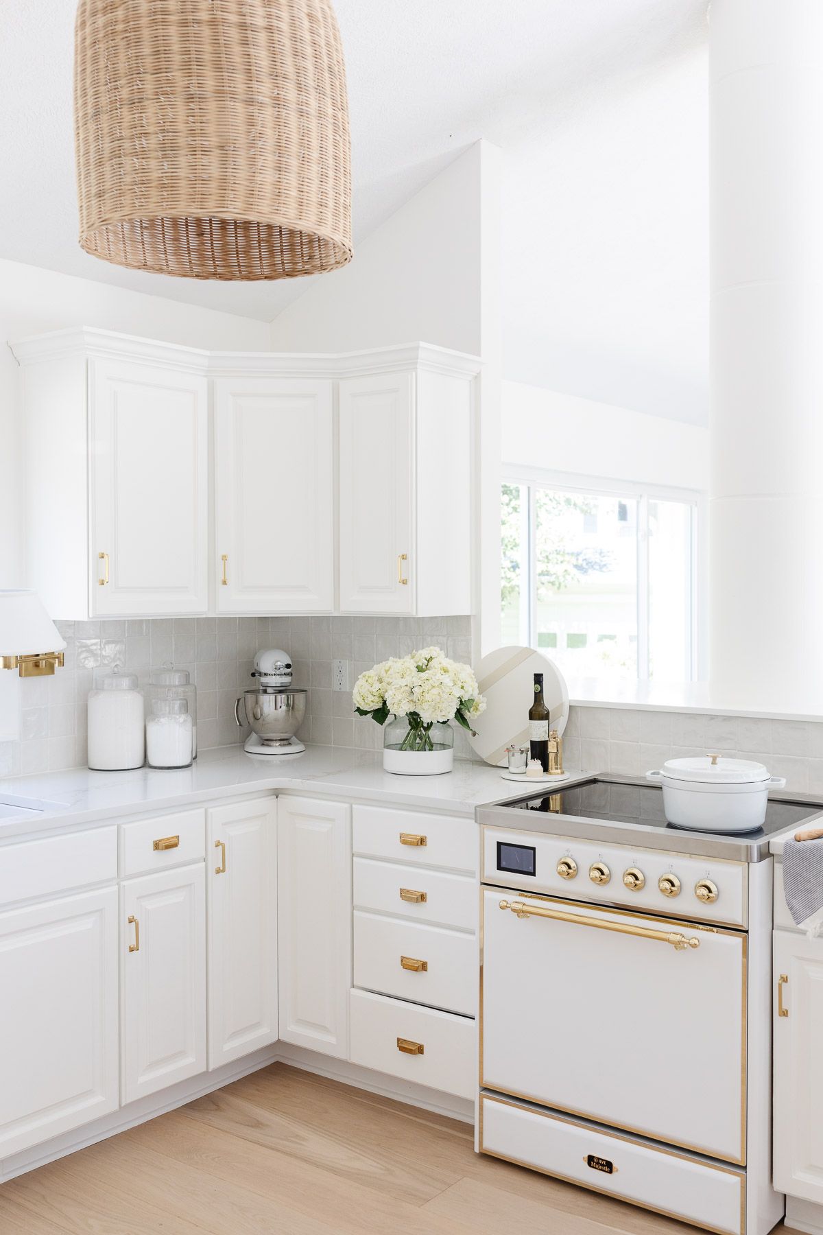 A white kitchen with wood floors, featuring a white ILVE Majestic II range