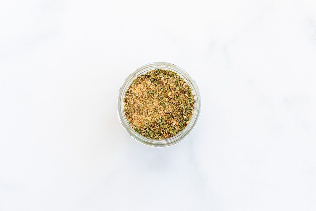 A small glass container filled with all-purpose seasoning placed on a marble table top.