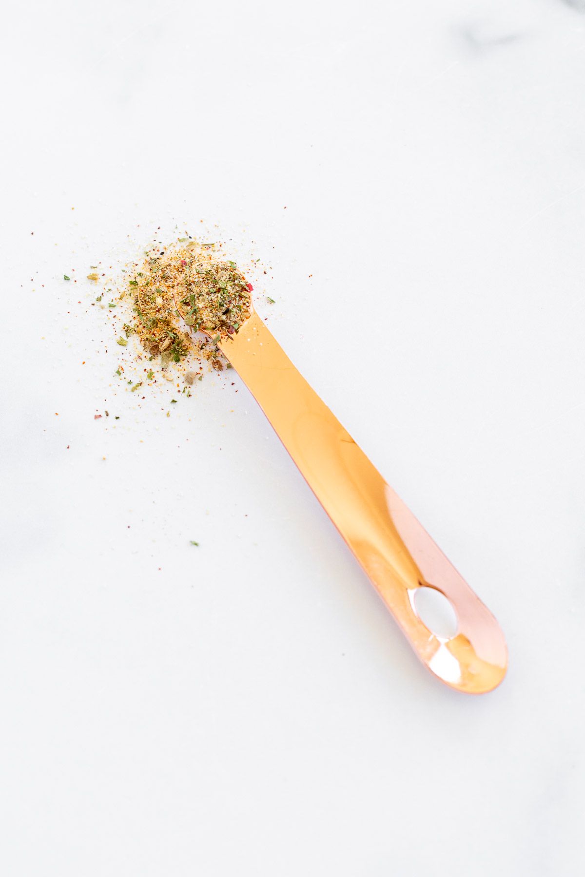A copper teaspoon placed on a marble table top with all purpose spice.