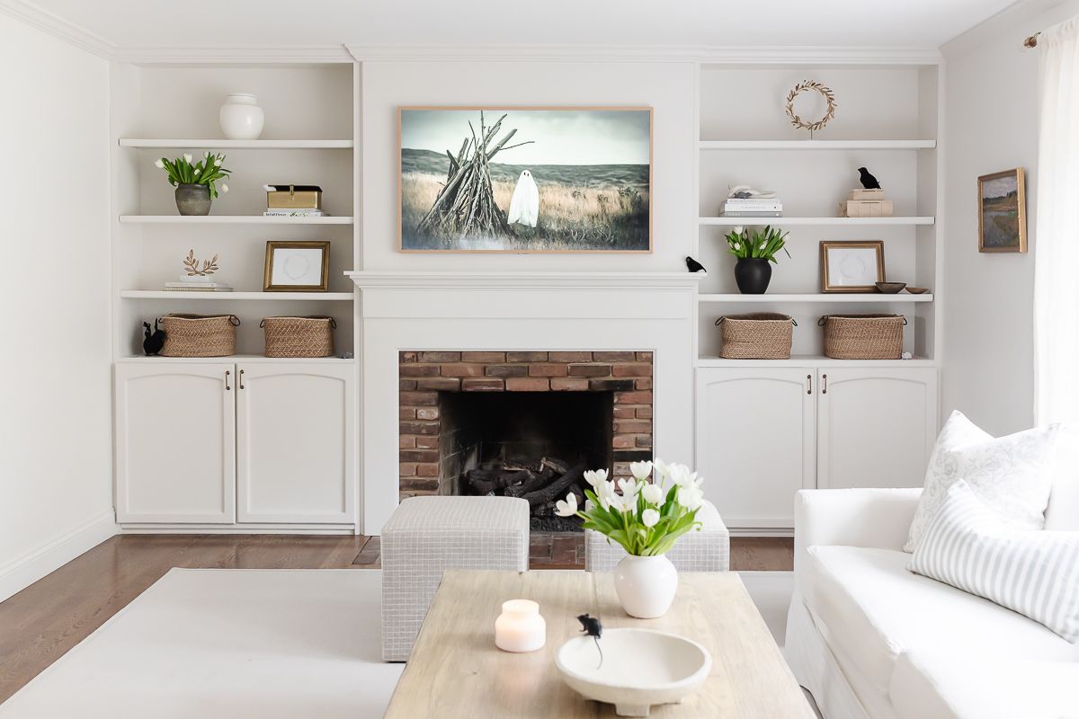 A white living room decorated with Amazon Halloween decor elements, with a spooky scene on the TV over the mantel