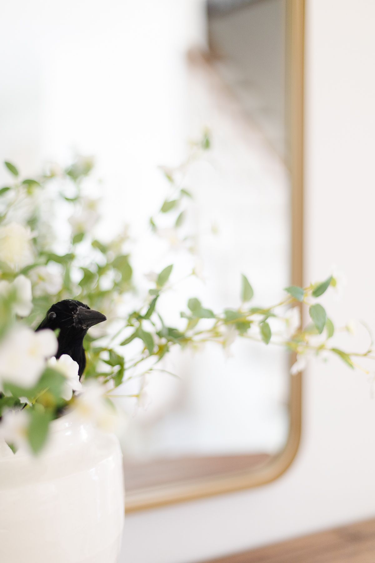 A black crow hiding in a white vase of flowers for halloween decor