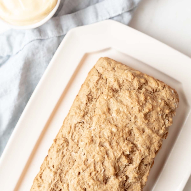 A loaf of beer bread on a white platter, with a small jar of honey butter to the side.