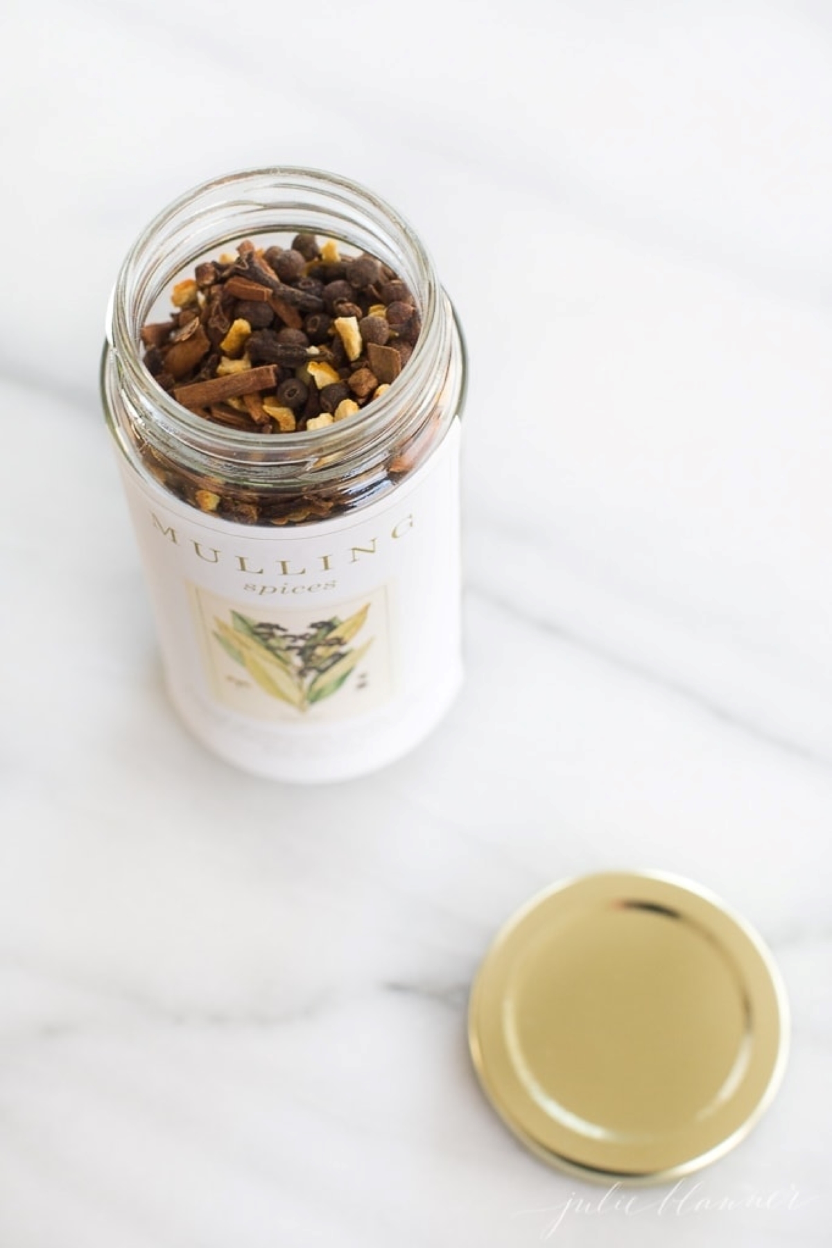 A bottle of mulling spices resting on a marble countertop, gold lid to the side.