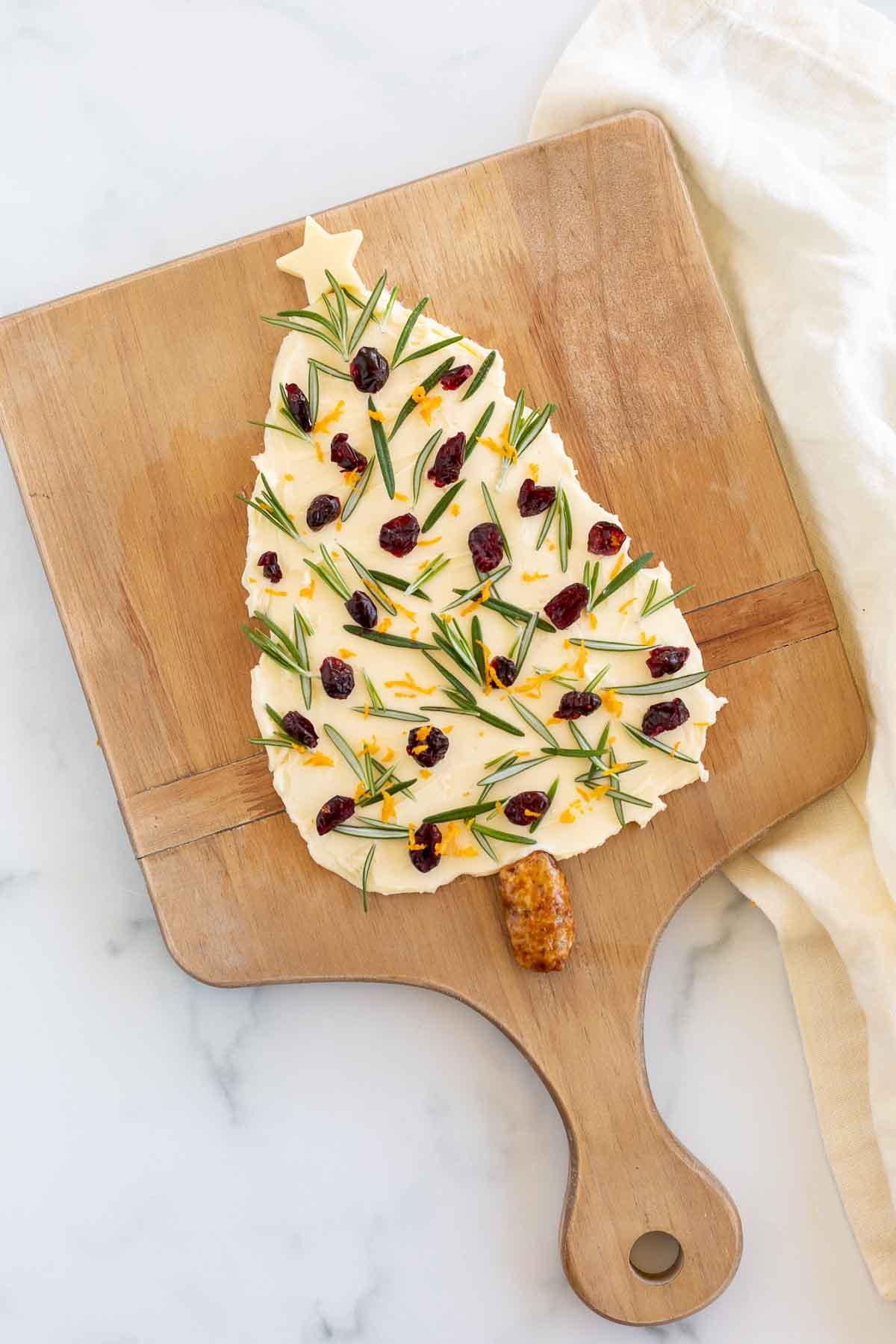 A butter board shaped into a Christmas tree, placed on a wooden board. 