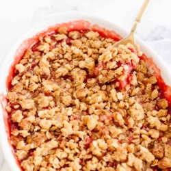 A strawberry crumble, topping with a crumble topping with oats, gold spoon to the side
