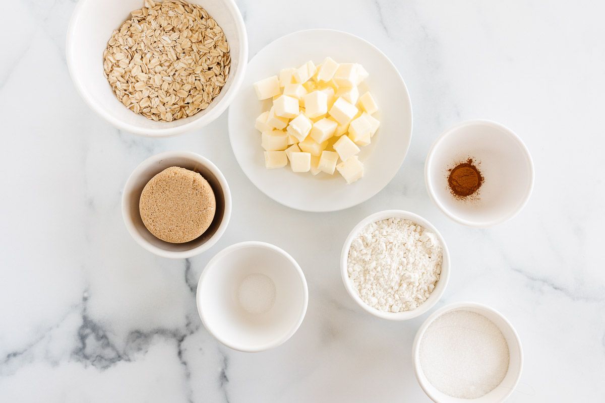 Ingredients for a crumble topping with oats, laid out on a marble countertop.