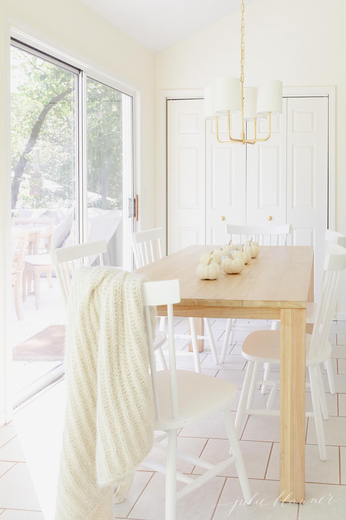 A white kitchen with a teak table, cozy blanket draped across the back of a chair