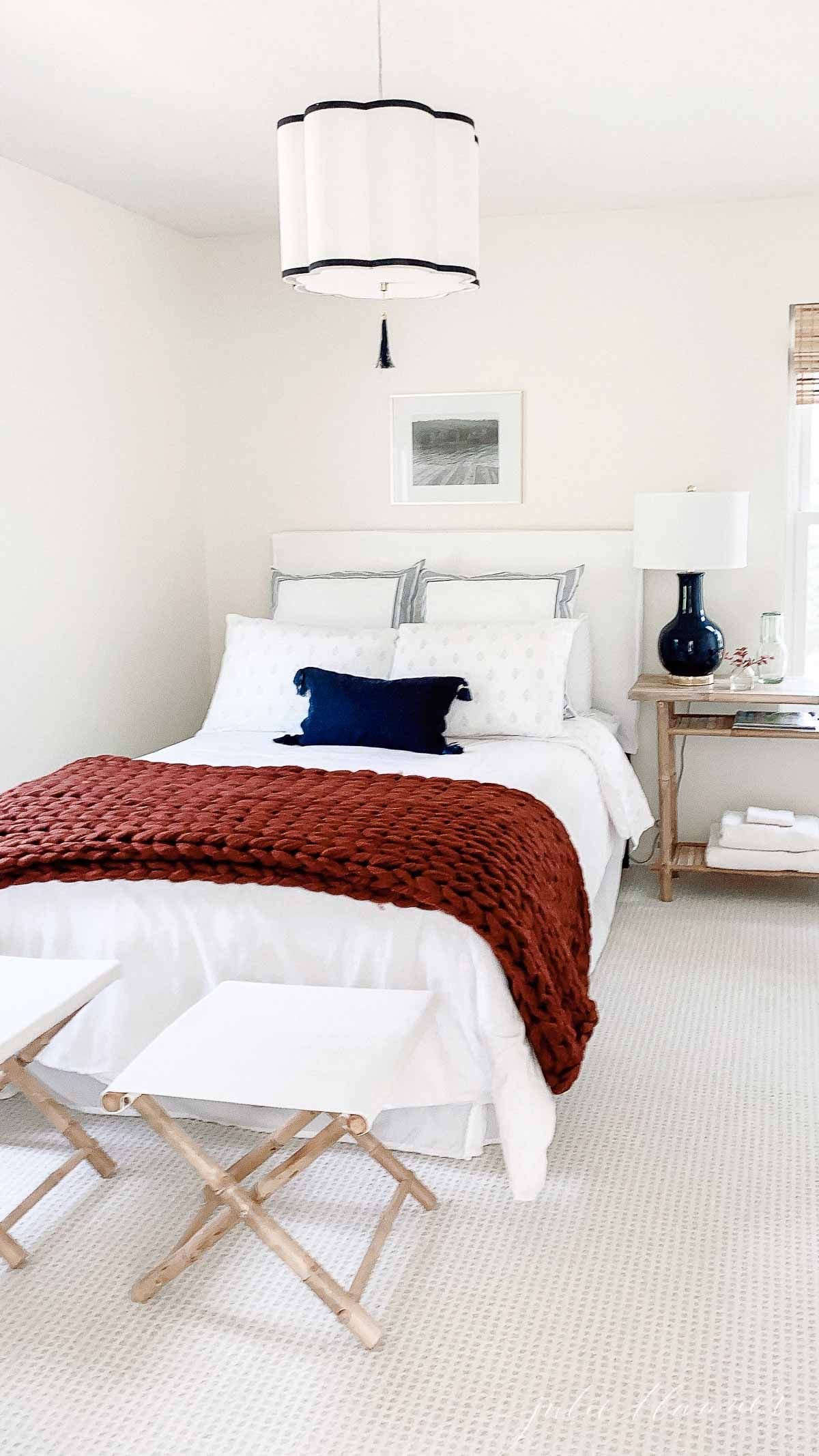 A white guest bedroom featuring a cozy burgundy knit blanket for a fall decor idea