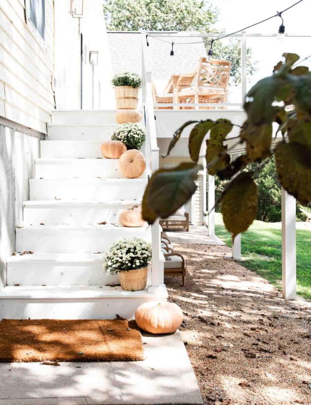 A white deck with steps that have fall decor ideas like white mums and pumpkins