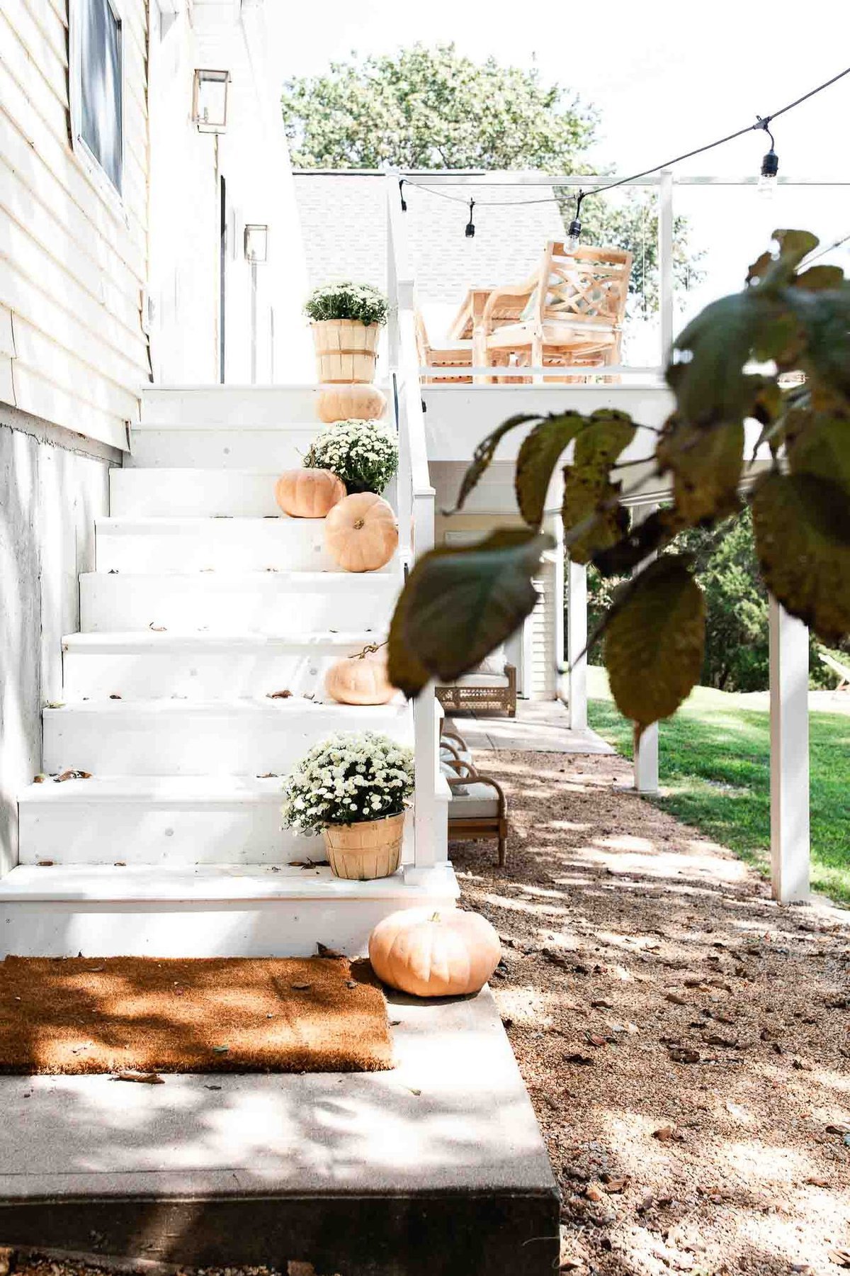 A white deck with steps that have fall decor ideas like white mums and pumpkins 