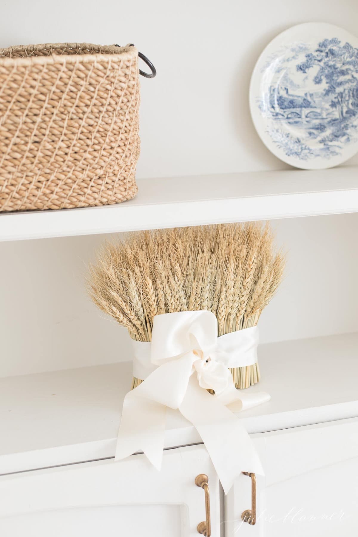 A wheat sheaf tied with a white bow on some white bookcases styled for fall