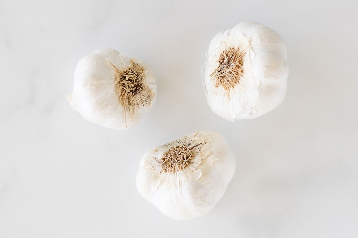Three full cloves of garlic, placed on a marble table top.
