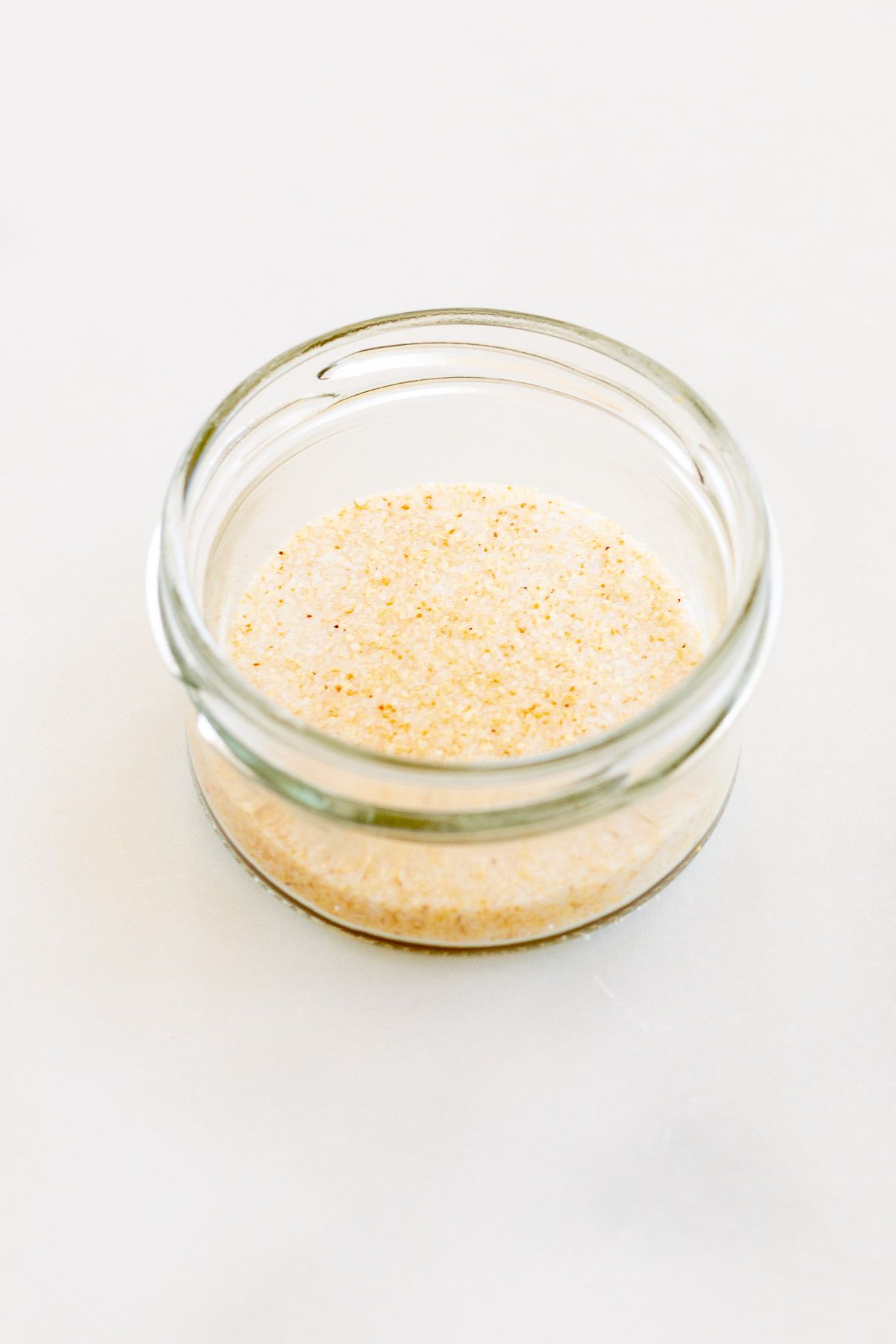 A small glass jar filled with homemade garlic salt, placed on a marble countertop.