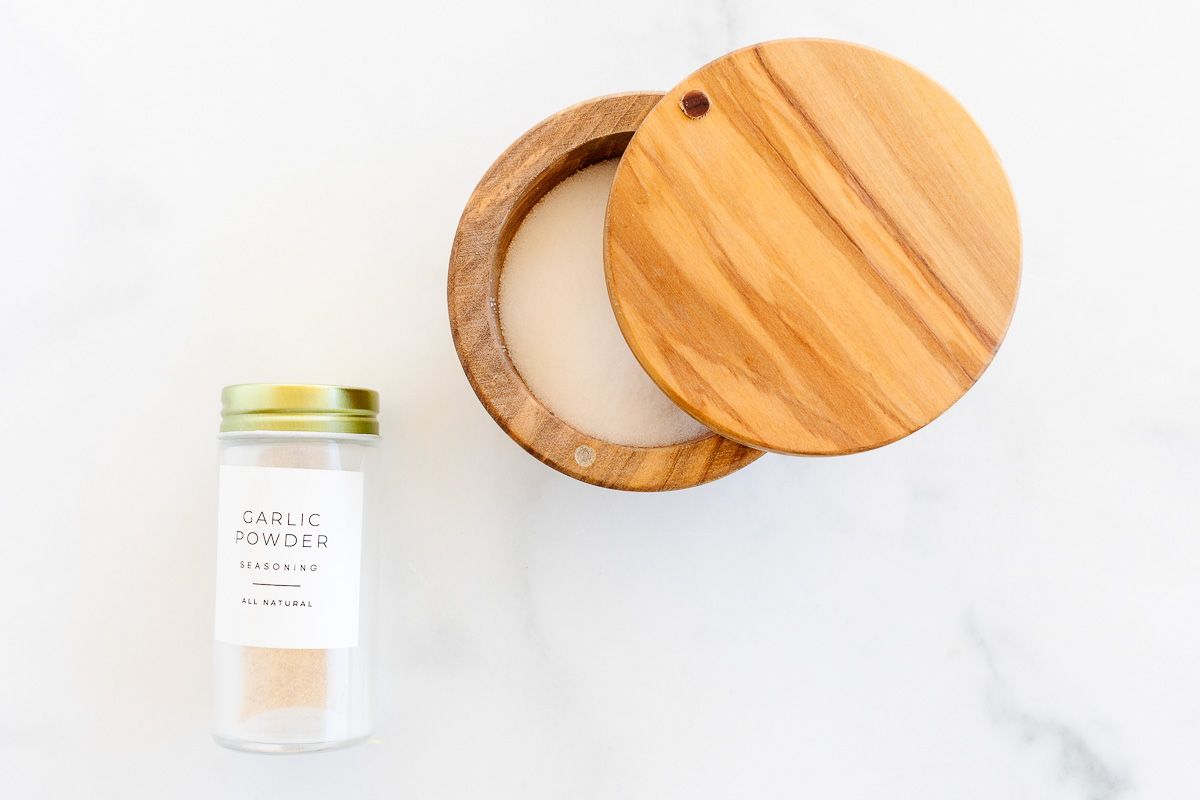 A homemade garlic salt blend in a small wooden salt cellar, with a glass bottle of garlic powder to the side.