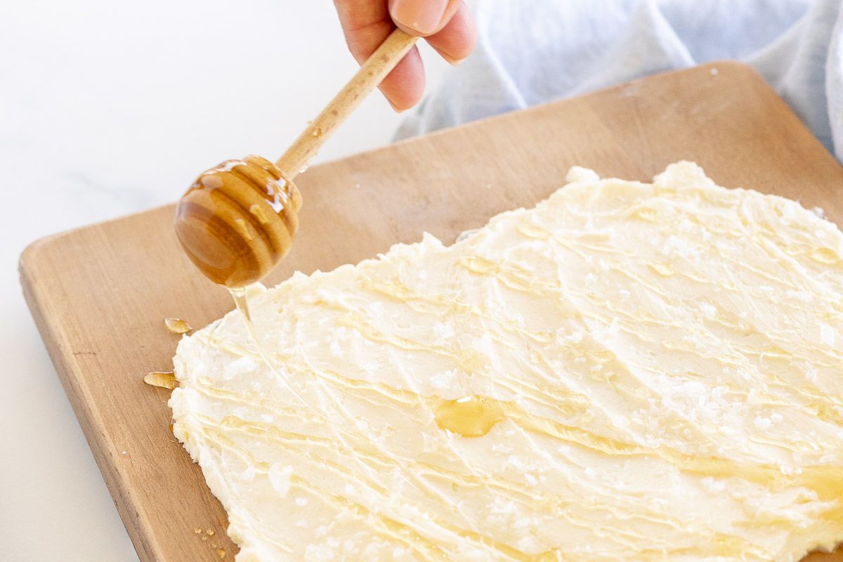 The beginning of a butter board, with a blue linen towel in the background, honey being drizzled over the top