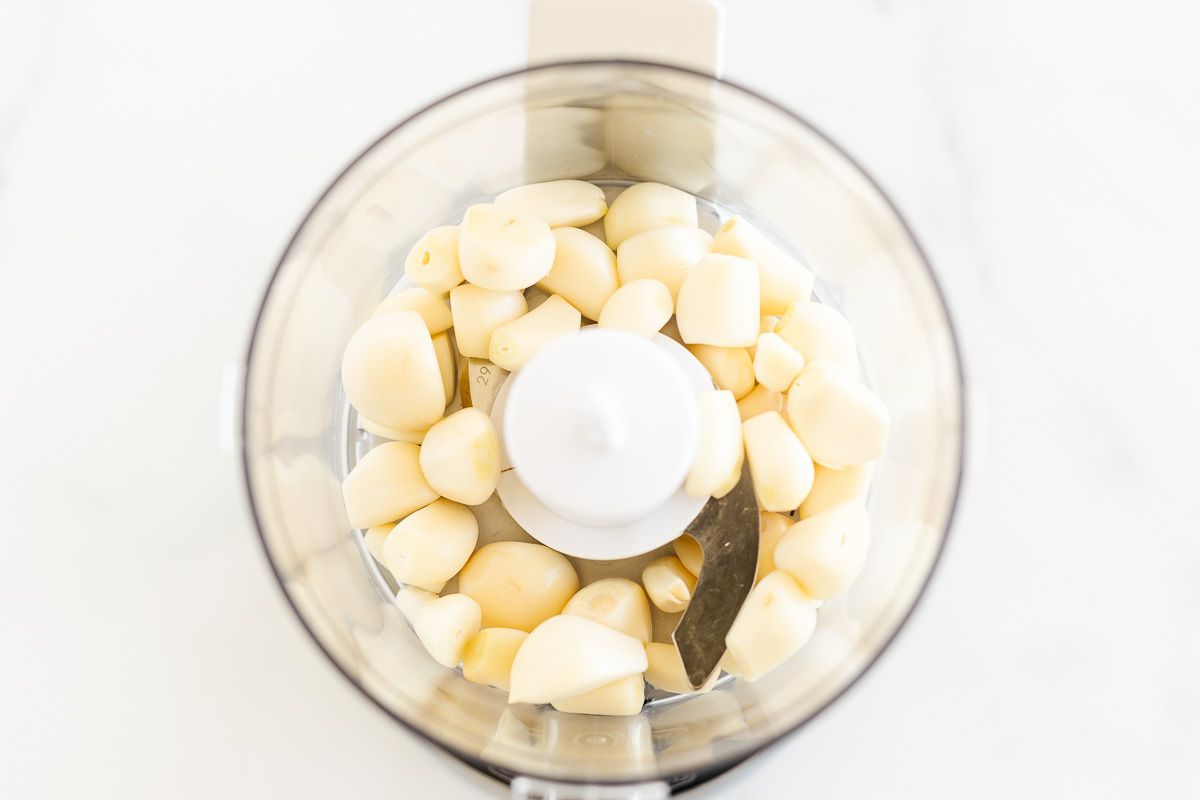 Looking inside a food processor, filled with garlic bulbs for a tutorial on how to make garlic paste.