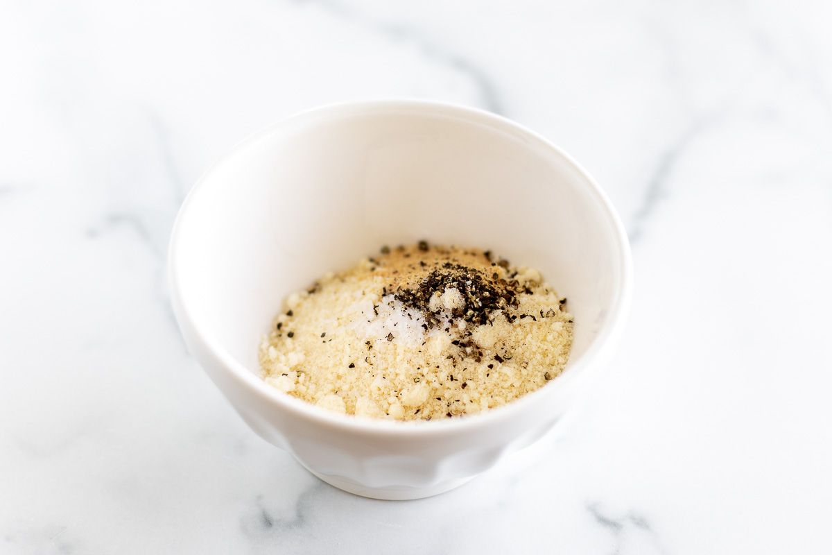 Parmesan and spices in a white bowl, on a marble surface.