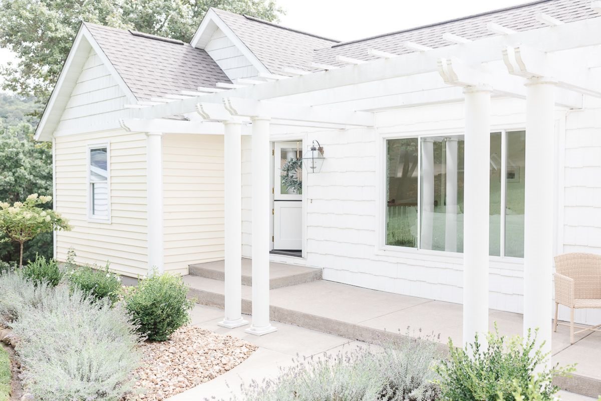 Exterior of a lake cottage with a white pergola over the front porch.