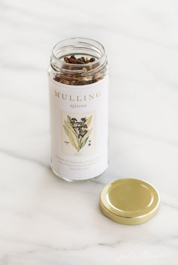 A bottle of mulling spices resting on a marble countertop, with a gold lid to the side.